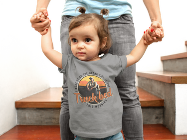 A young child wearing a gray t-shirt with a graphic design and text, standing in front of an adult who is holding their hands.